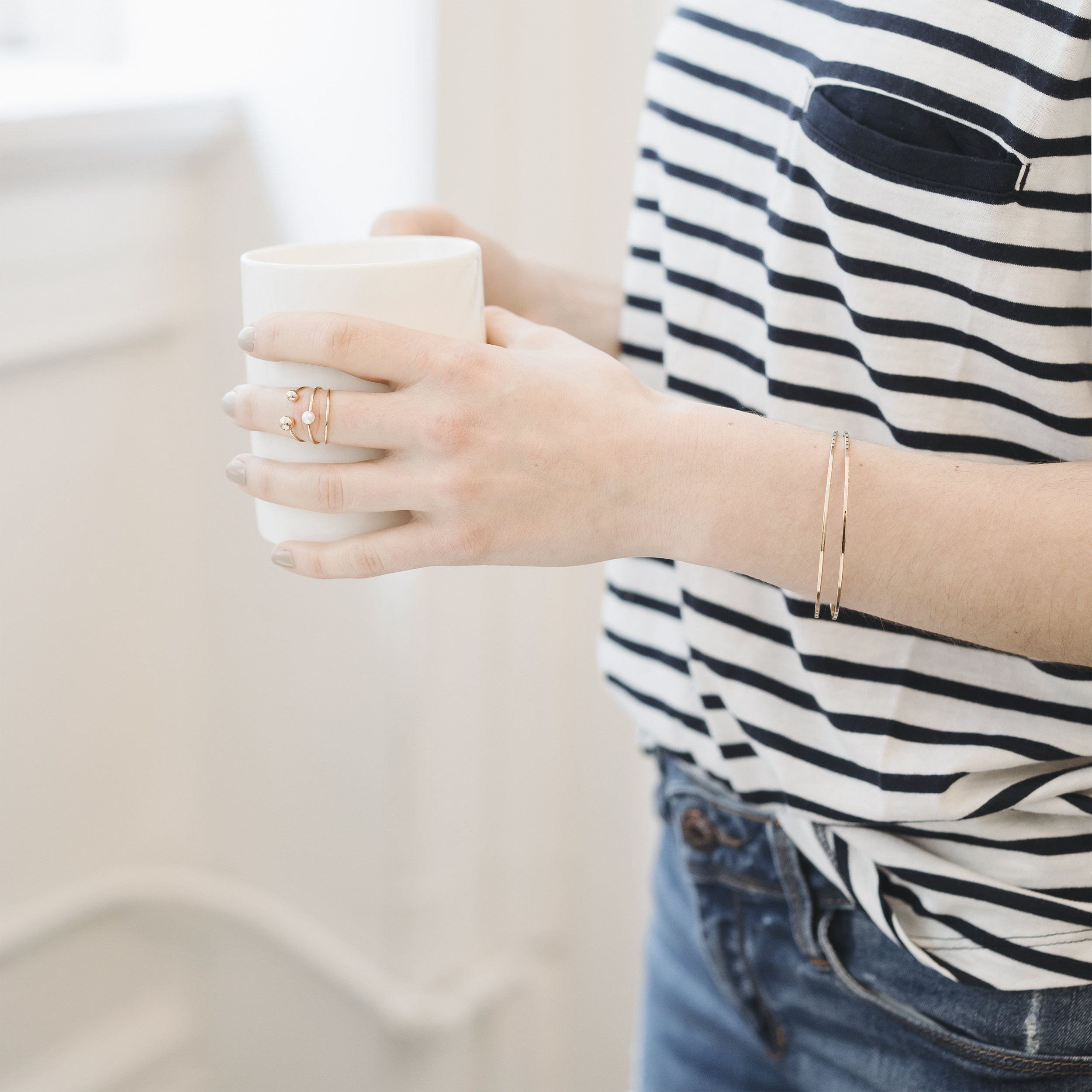 Casually dressed lady holding a white ceramic cup of coffee., standing in a bright pretty room