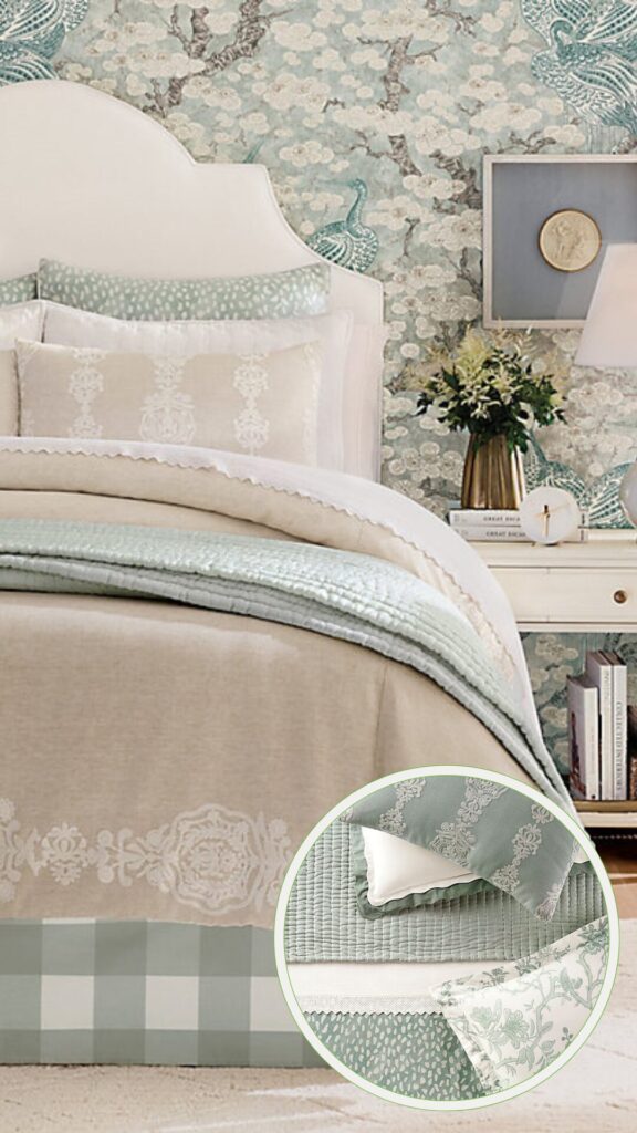 A cozy bedroom featuring luxe bedding with embroidered details and soft layers in cream and mint tones. The bed is framed by a scalloped headboard and set against a whimsical wallpaper backdrop. A white nightstand with a lamp and decor completes the inviting look.